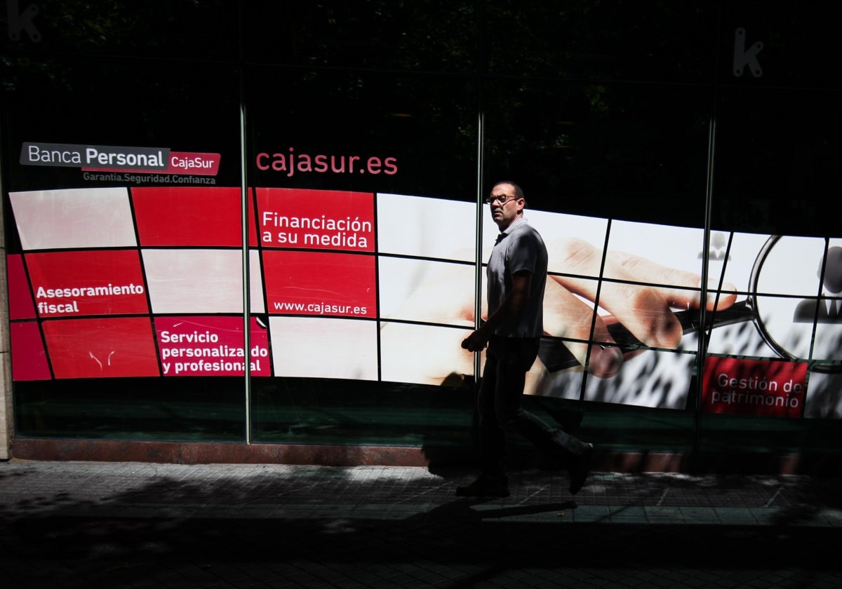 Un viandante pasa por un panel promocional de Cajasur en una de sus sedes en Córdoba