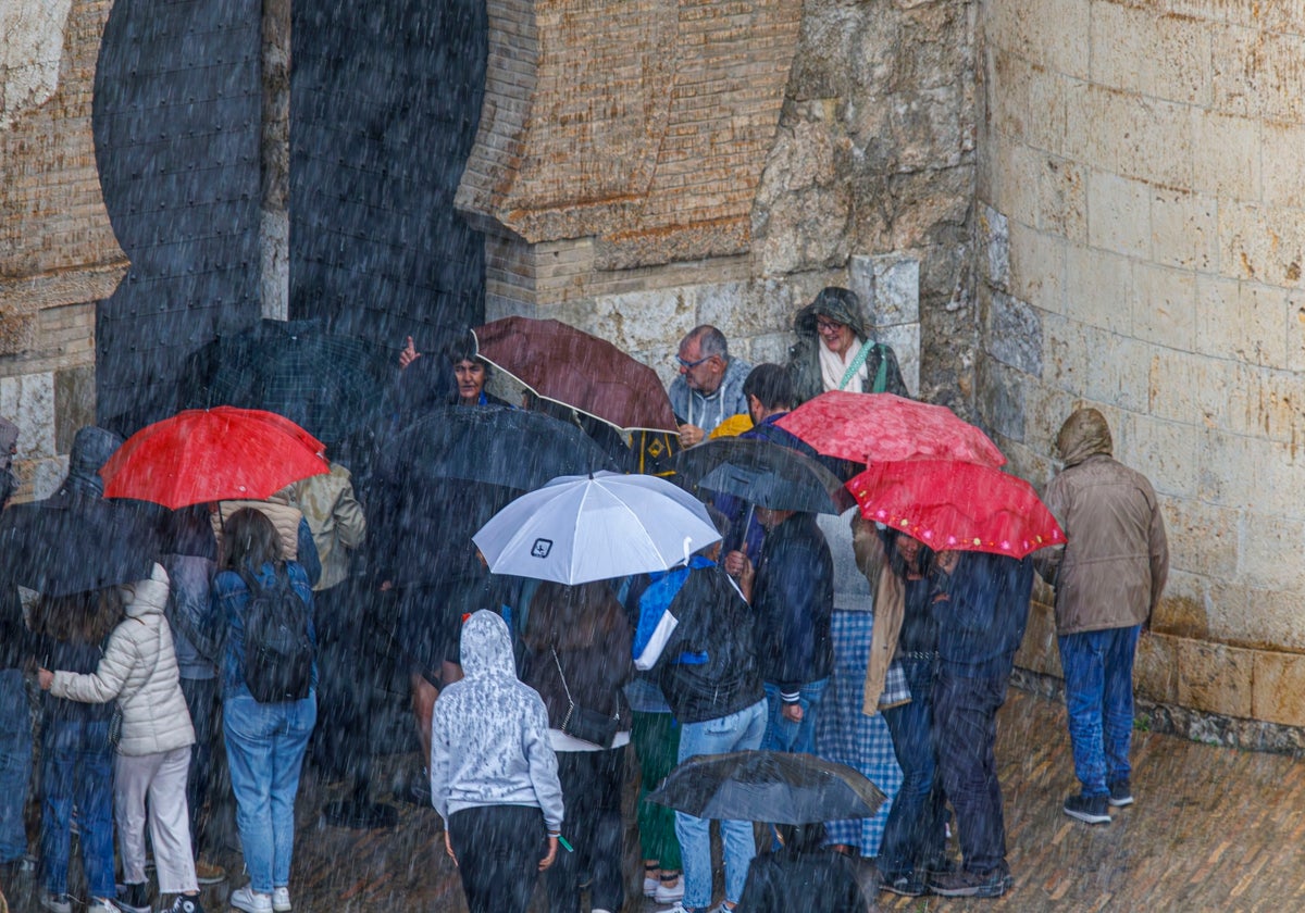 Turistas a las puertas del palacio de La Aljaferia se protegen del chaparrón de este viernes en Zaragoza